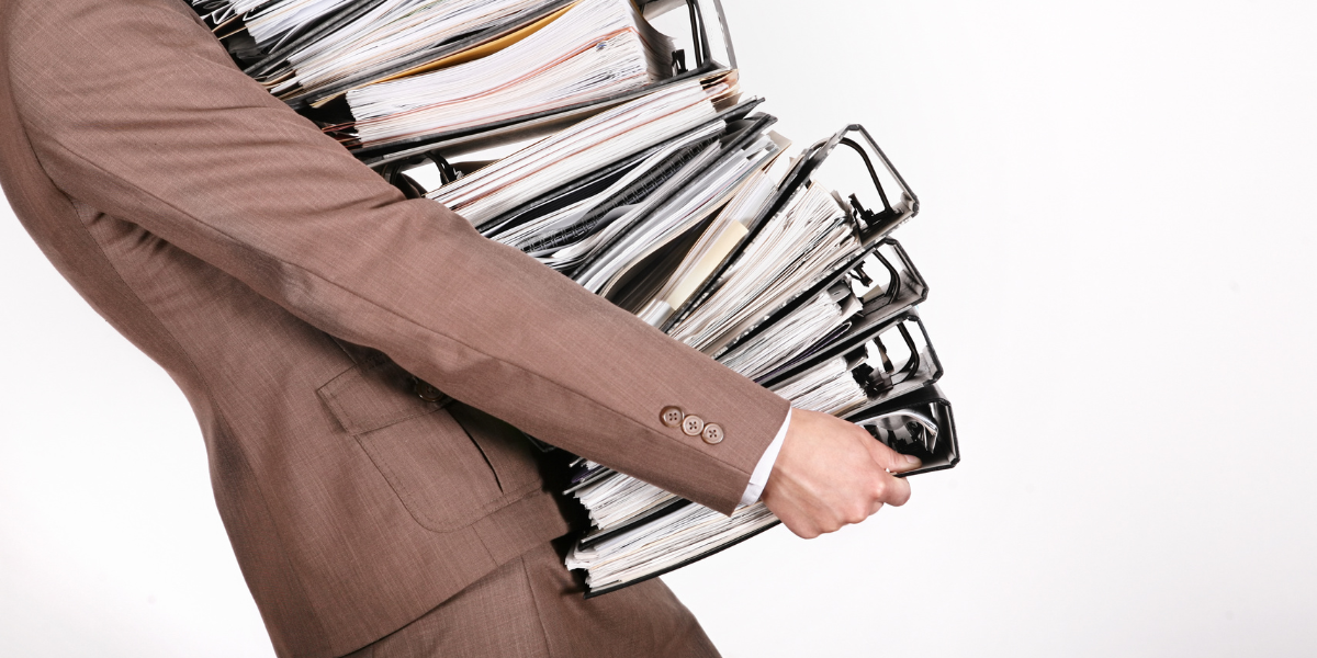 Businessman struggling with large stack of file folders, a problem that could be avoided by using paperless office methods. 