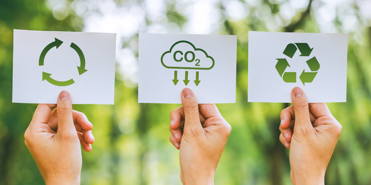 Three hands hold up cards that indicate features of eco-friendly printing. Two have reduce, reuse, recycle symbols and the third has a reduce CO2 symbol on it.