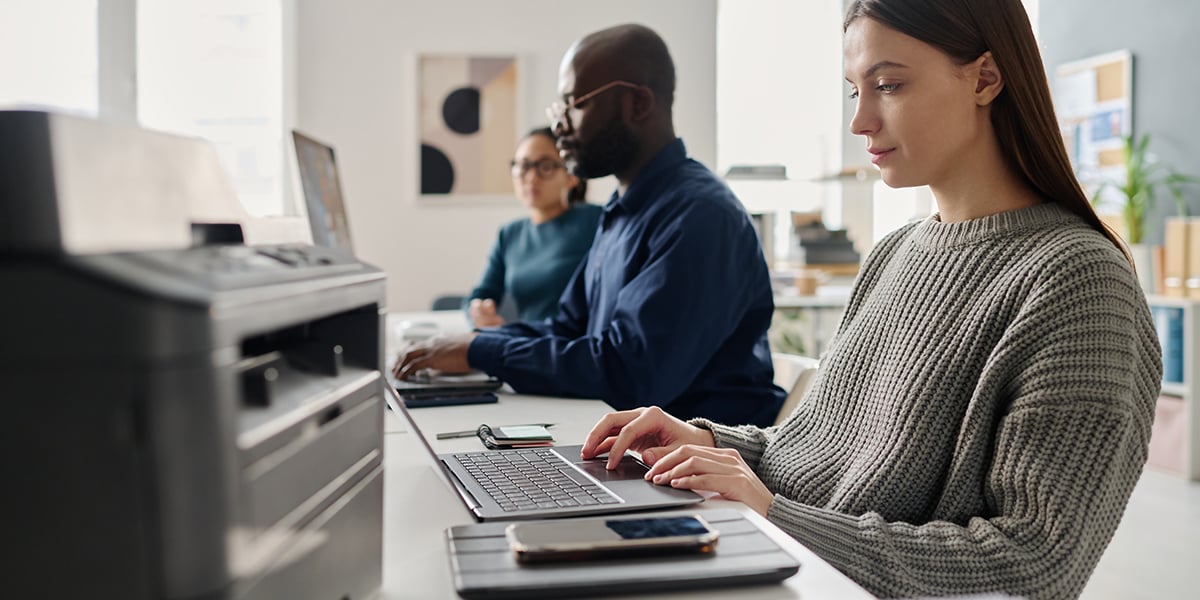group of coworkers working on laptops with a printer sitting on the table
